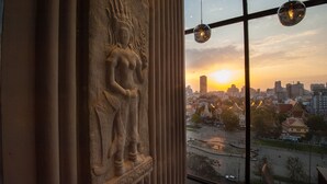 En statue af en guddom, et bybillede med bygninger, og en solnedgang gennem et vindue med gardiner.
