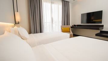A hotel room with two beds, a television mounted on the wall, a desk with a mirror, and a window with curtains.