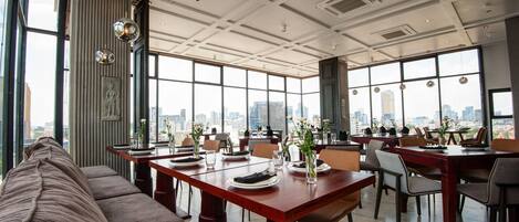 Un comedor amplio con ventanas grandes que ofrecen vista a la ciudad, mobiliario moderno y espejos decorativos.