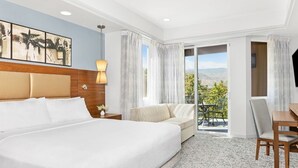 A hotel room with a large bed, a sofa, a desk, and a balcony with a view.