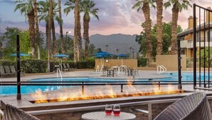A pool area with lounge chairs, a fire feature, and a view of mountains.