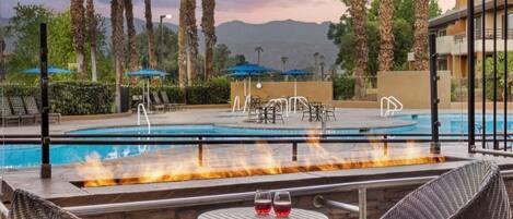 A pool area with lounge chairs, a fire feature, and a view of mountains.