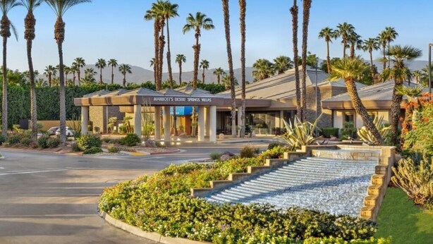 A hotel with a modern design, palm trees, and a landscaped area with steps leading to the entrance.