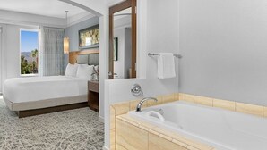 A hotel room with a large bed, a separate bathroom with a bathtub, and a view of the outdoors.