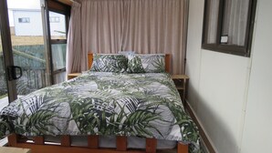 A bedroom with a bed, a window, and a curtain. - Sandy Toes and Salty Kisses (Coopers Beach)