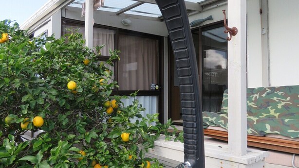 A covered outdoor area with a metal structure, a bush with yellow fruits, and a white bucket labeled "Resen". - Sandy Toes and Salty Kisses (Coopers Beach)