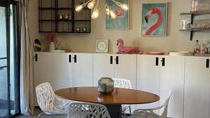 A modern kitchen with white cabinets, a round wooden table, and white chairs. There is a decorative light fixture above the table and a painting of a flamingo on the wall. - Great Palm Springs Oasis 2 miles from downtown! (Palm Springs)