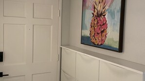 A hallway with a white door, a white wall, and a framed painting of a pineapple. - Great Palm Springs Oasis 2 miles from downtown! (Palm Springs)