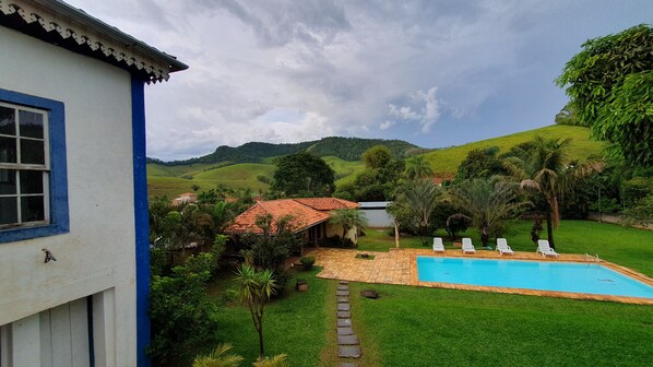 A pool area with a tiled deck, surrounded by lush greenery and hills in the background.