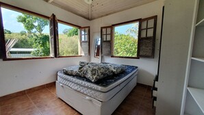 A bedroom with a bed, two windows with shutters, and a view of greenery outside.