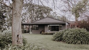 Une maison dotée d’un porche abrité, d’une pelouse et d’une végétation luxuriante tout autour.