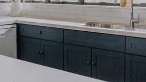 Une cuisine avec une grande fenêtre, un évier et un vase rempli de fleurs posé sur le plan de travail.