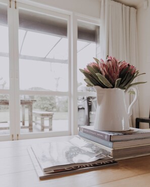 A white pitcher with pink flowers on a table, next to a window with a view of a snowy landscape. - Moomaa Stay - Rural Delight (Marton)