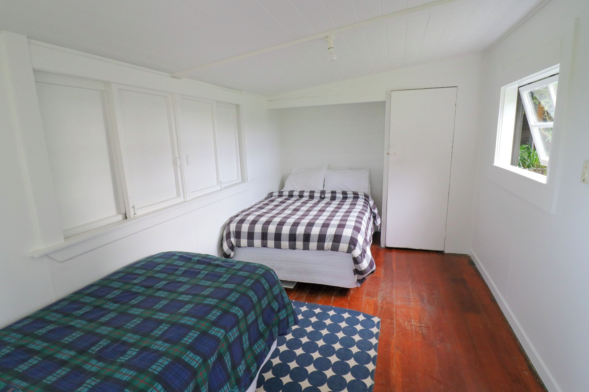 Una habitación pequeña y blanca con dos camas, una ventana y suelo de madera.