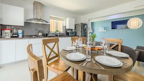 A modern kitchen with white cabinets, a stainless steel range hood, and a dining area with a round table set for four. - Koyari Modern Condos 3 w Private Roof Deck (Noord)