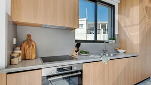 Ett modernt kök med träskåp, en ugn från Bosch, ett fönster med utsikt över byggnader och en bänkskiva med en skärbräda, en knivuppsättning och några burkar.