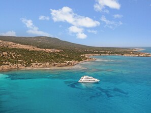 A white yacht on clear turquoise waters with a coastline and hills in the background. - Sanders Olive - Cozy 2-bdr Apt With Shared Pool (Paphos)