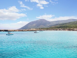 A coastal scene with clear turquoise waters, rocky cliffs, and mountains in the background. - Sanders Olive - Cozy 1-bdr Apt With Shared Pool (Paphos)