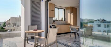 Un apartamento moderno con balcón, un comedor con mesa y sillas redondas y una cocina con armarios de madera y una ventana.