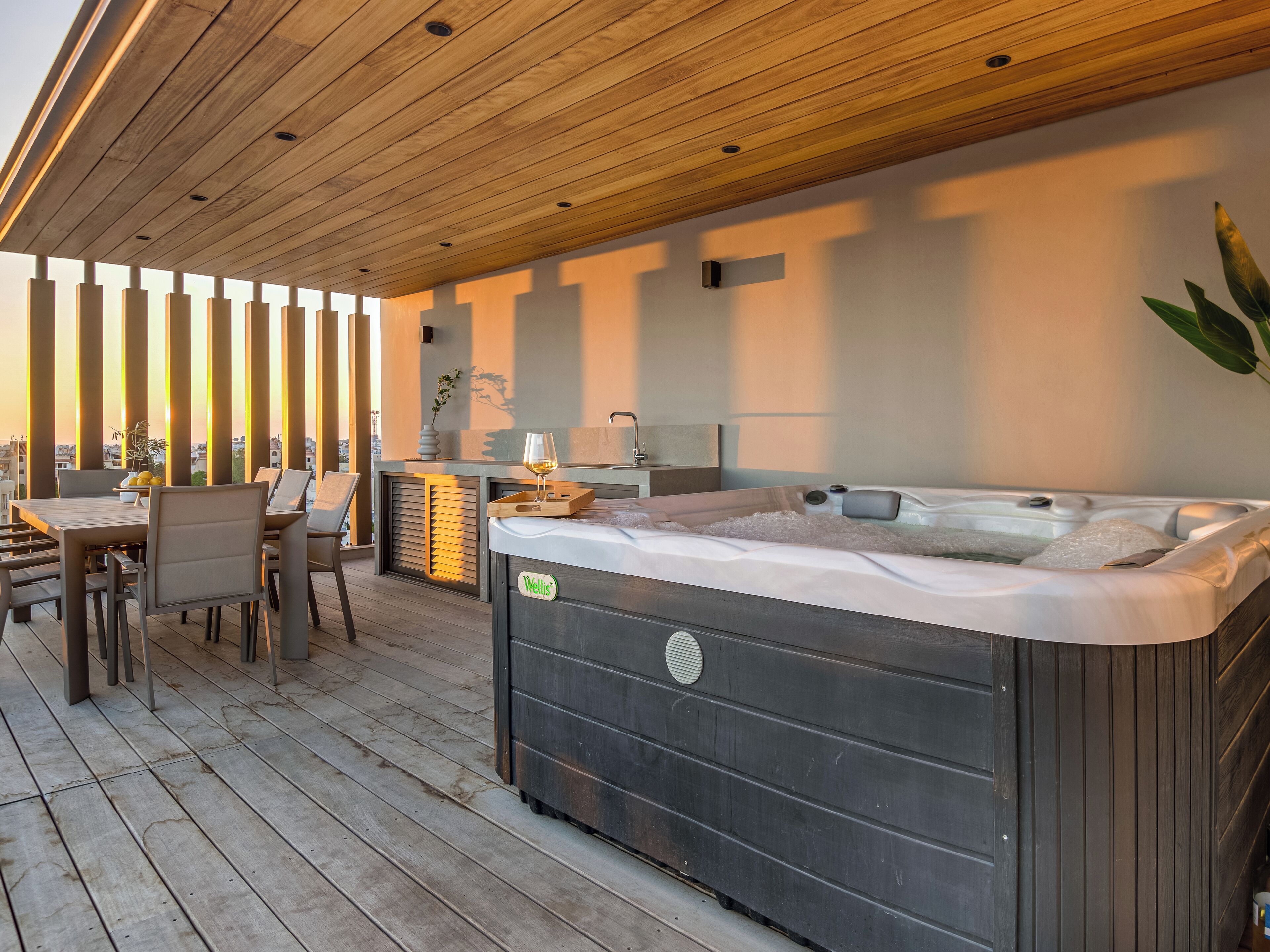 Un bain à remous avec une terrasse en bois, une table et des chaises, et une vue sur le paysage urbain.