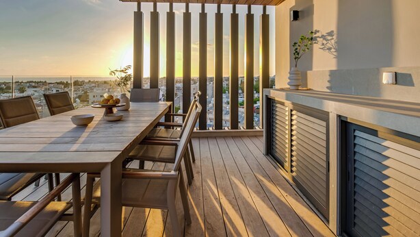 Terraza de madera con mesa y sillas, con vistas a un paisaje urbano al atardecer.