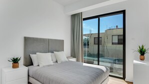 Un dormitorio moderno con una cama grande, una mesita de noche, una pequeña planta en maceta y vistas al exterior a través de un ventanal corredero.