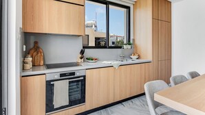 Una cocina moderna con armarios de madera, horno empotrado, lavamanos y ventana con vistas a la ciudad.