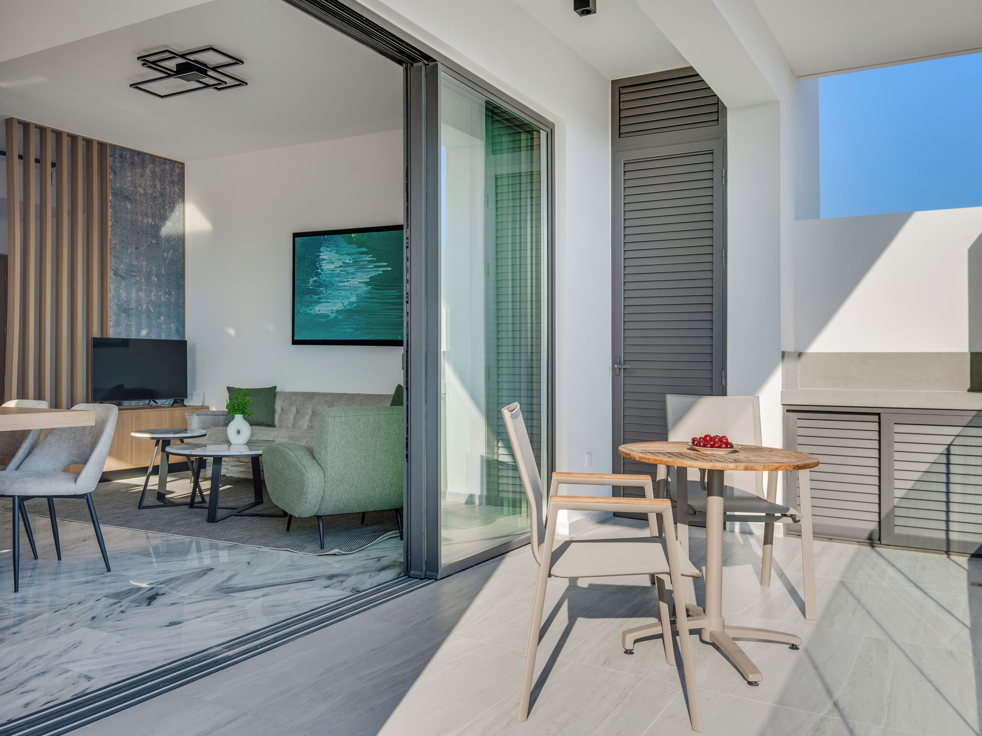Ein moderner Wohnbereich mit Glastür zu einem Balkon, einem Flachbildfernseher, einer Couch und einem Essbereich mit Stühlen und Tisch.