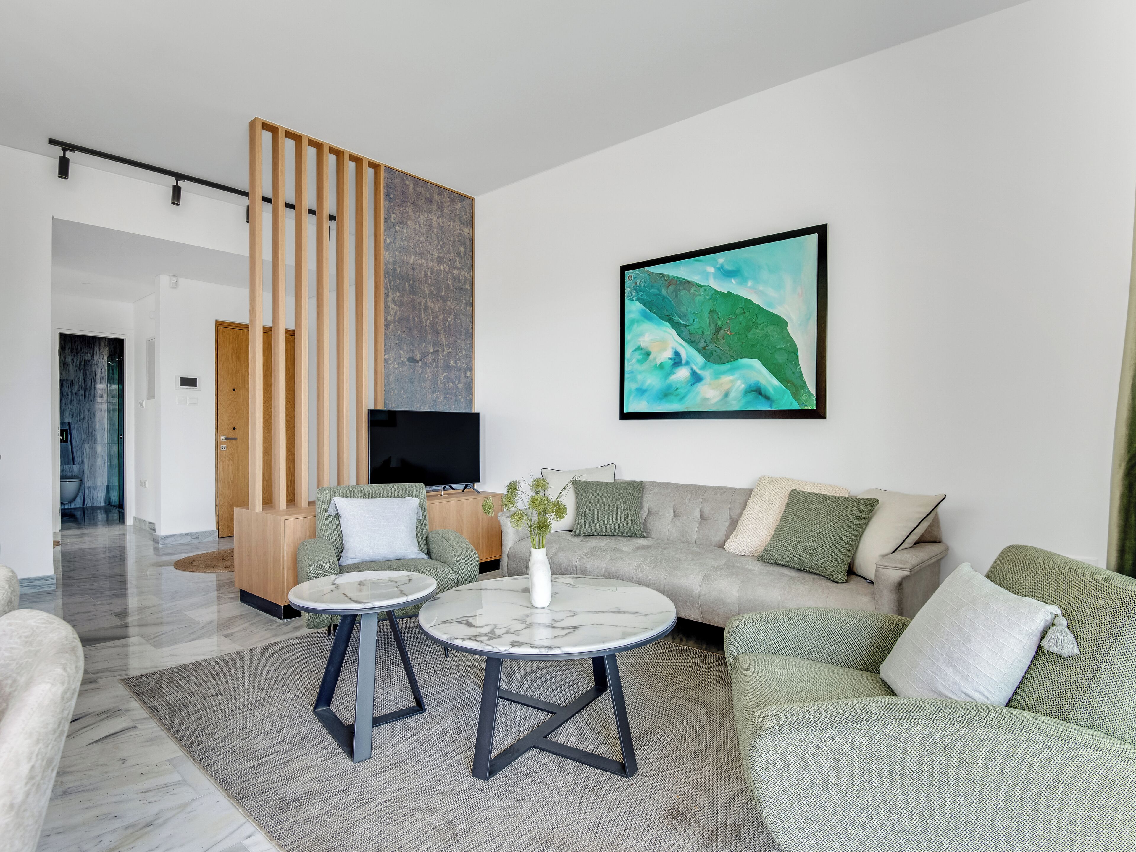 A modern living room with a large sofa, two side tables, a flat-screen TV, and a large abstract painting.