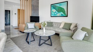 Ett modernt vardagsrum med en stor soffa, två sidobord, en platt-TV och en stor, abstrakt tavla.