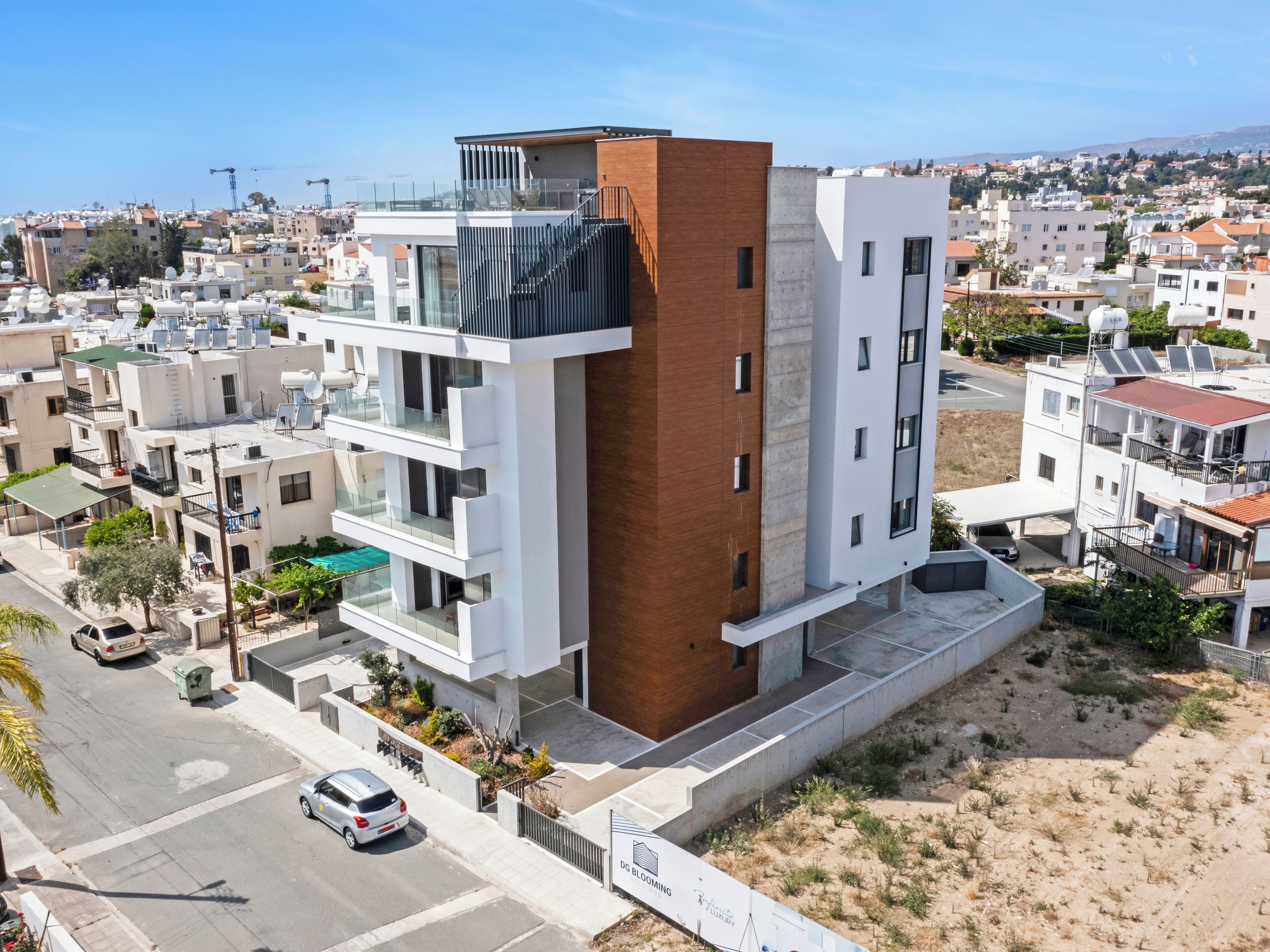 Un edificio moderno de varios pisos con balcones, una terraza en la azotea y un jardín ajardinado con plantas.