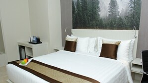 A hotel room with a bed, a nightstand with a coffee maker, and a view of a forest through a window. - Horison Abepura (Jayapura)