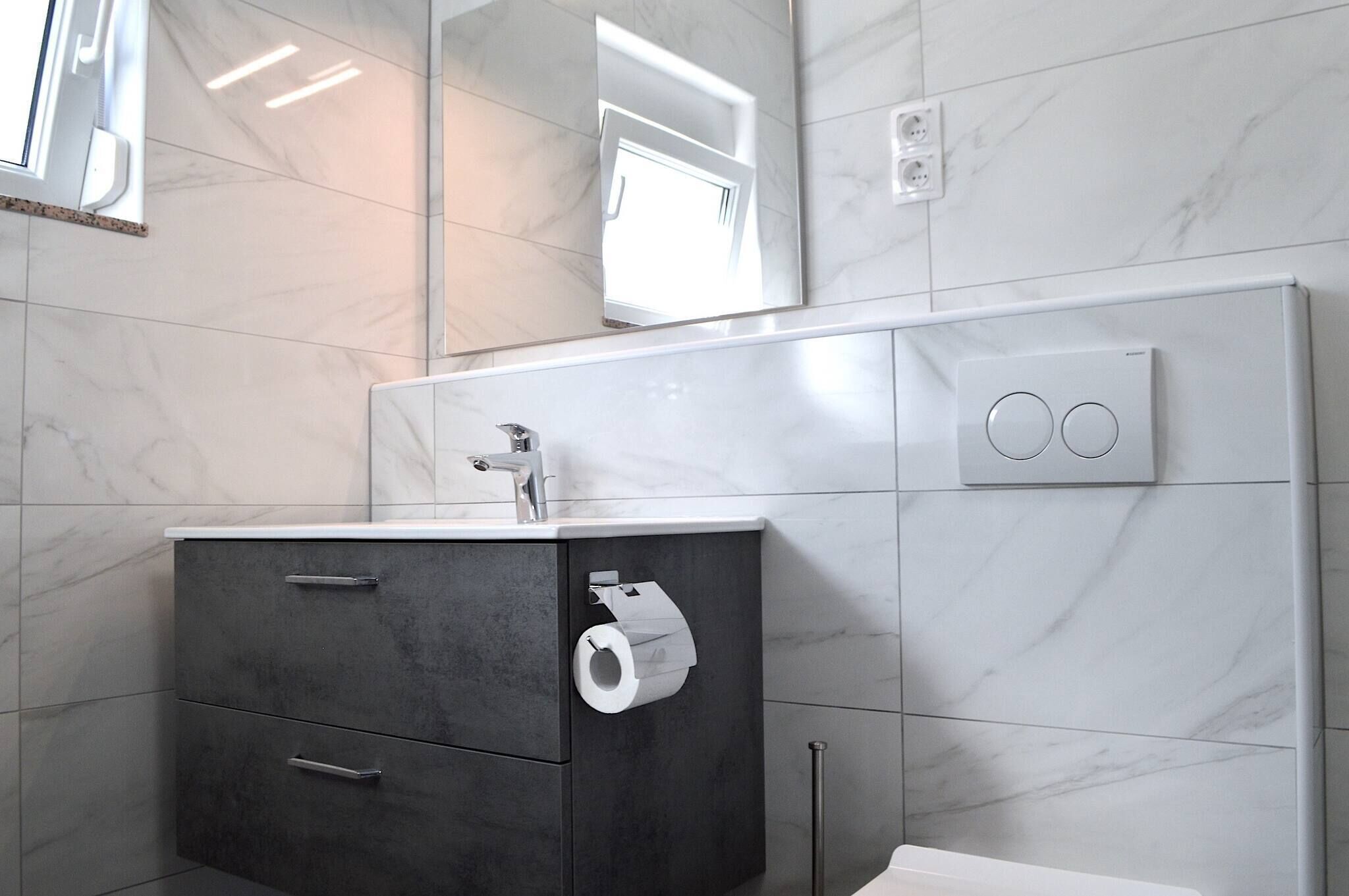 A modern bathroom with a marble-tiled wall, a dark-colored vanity with a faucet, a toilet paper holder, and a mirror.