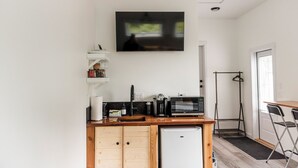 A compact kitchen with a microwave, coffee maker, and a small refrigerator. There is a wooden cabinet below the counter and a TV mounted on the wall. - *Getaway Private Suite "El Faro" (Ucluelet)