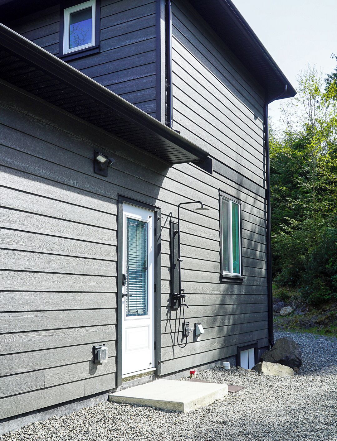 Un bâtiment à deux étages, à l’extérieur gris, avec une porte blanche et un petit porche.