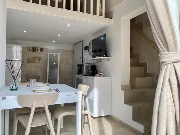 Een compacte woonruimte met een eethoek, kitchenette en een aan de muur bevestigde televisie.