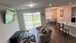 A modern living room with a sofa, TV, and a dining area with chairs and a table. - Beautiful and spacious 4BR house in Port St. Lucie, FL (Port St. Lucie)
