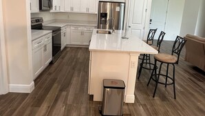 A modern kitchen with white cabinets, stainless steel appliances, and a central island with bar stools. - Beautiful and spacious 4BR house in Port St. Lucie, FL (Port St. Lucie)