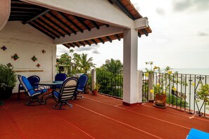 Une terrasse extérieure couverte, avec une table et des chaises, des plantes en pot et une vue sur l’océan.