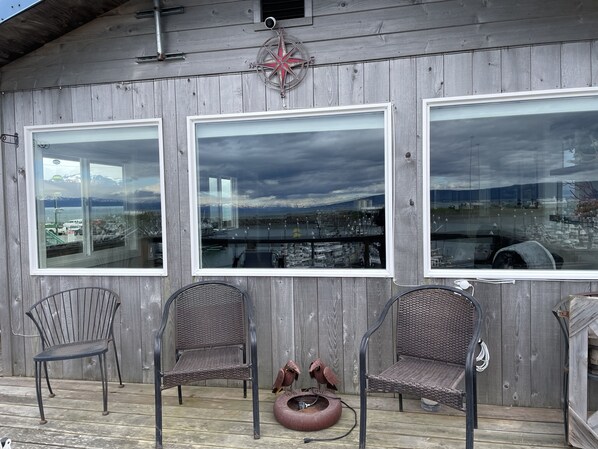 A wooden deck with three wicker chairs and a bird sculpture. - Beautiful Homer Spit Vacation Rental Overlooking Harbor (Homer)