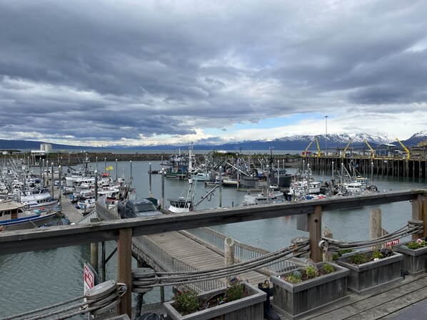 A marina with boats docked, a wooden pier, and a mountain range in the background.