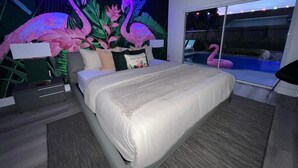 A modern bedroom with a large bed, a mural of flamingos, and a view of a pool. - Flamingo  Dream Escape / 5 Bedrooms/ Htd Pool/ Game Room/ BBQ / Baby items (Miami)