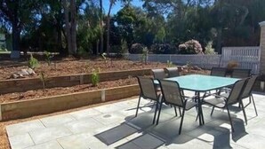 An outdoor patio with a table and chairs, surrounded by raised garden beds and trees.
