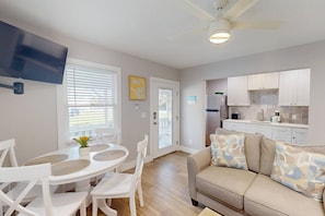 A modern kitchen with white cabinets, a built-in oven, and a refrigerator. There is a dining area with a white table and chairs, and a beige sofa with patterned cushions. - Walk to Beach & Johns Pass Village! Heated Pool ~ Private Patios ~ Free Parking & Amenities (Madeira Beach)