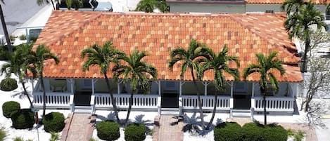 Un edificio con techo de tejas rojas, barandillas blancas y varias palmeras.