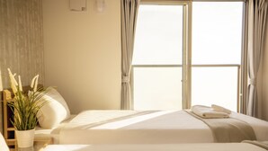 Une chambre d’hôtel avec deux lits, une plante en pot et une fenêtre avec des rideaux.