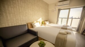 Une chambre d’hôtel avec un lit, un canapé, une petite table ronde agrémentée d’une plante et une grande fenêtre donnant sur un paysage.