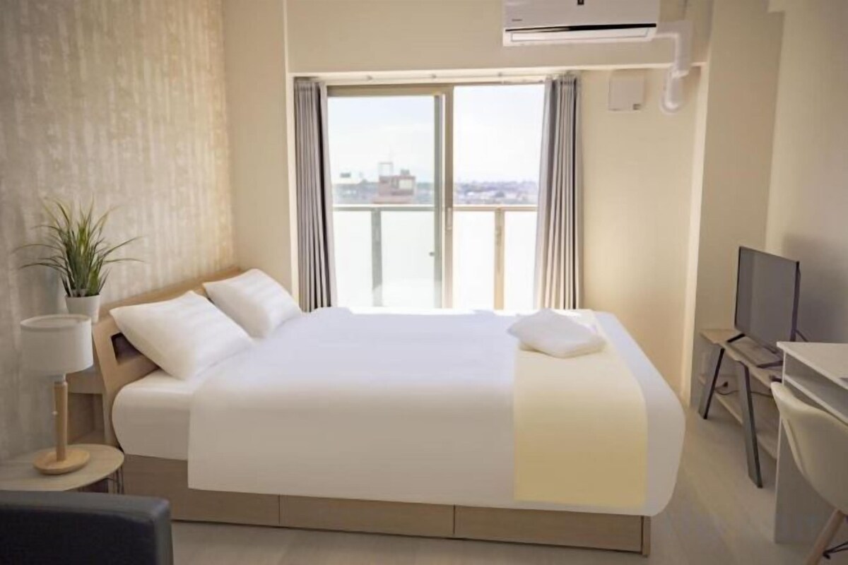 A hotel room with a large bed, a desk, a chair, a TV, and a window with a view.