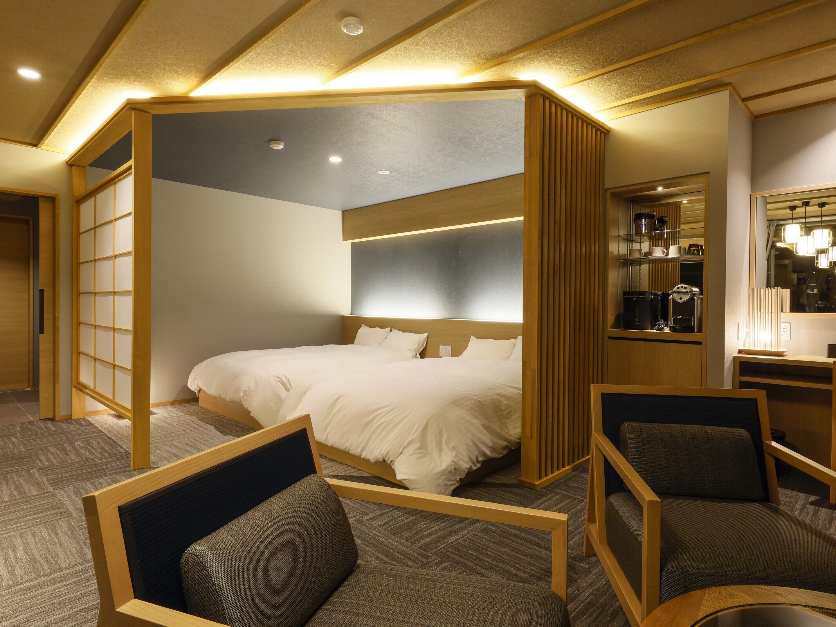 Une chambre d’hôtel avec un grand lit, un bureau avec une machine à café et un coin salon avec des fauteuils.