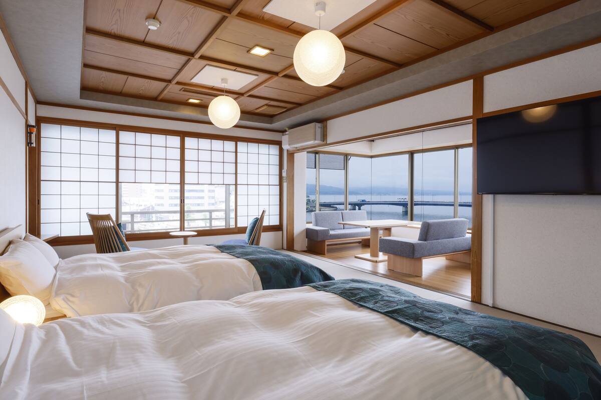 A hotel room with a large window, a sofa, a table, and two beds.